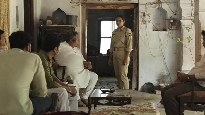 Santosh: An Indian female police officer stands talking to a room of five men