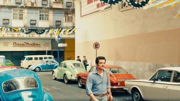 The Secret Agent movie: Wagner Moura walks through the streets of Brazilian city Recife with brightly colored cars parked either side of the road