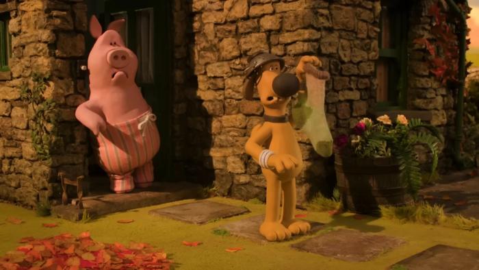 Shaun the Sheep—The Beast of Mossy Bottom: A dog holds a sock, while a pig watches from a stone house doorway, surrounded by autumn leaves