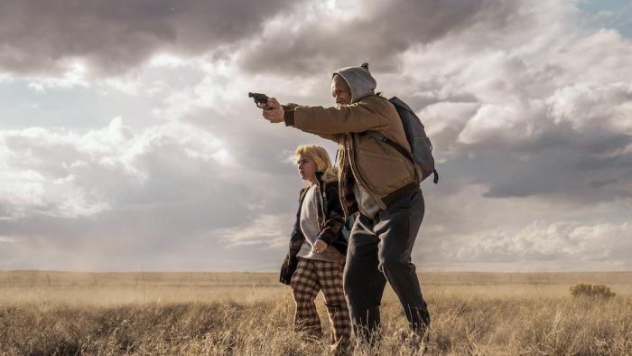 She Rides Shotgun Movie: Among the scrub brush and under a cloudy sky, Polly stands with Nathan, who aims a gun