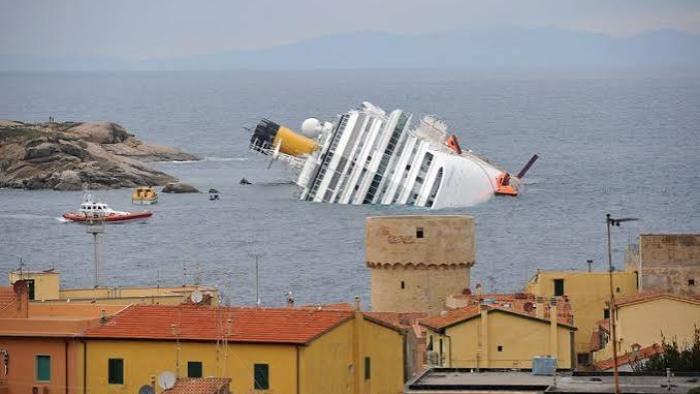 Shipwrecked: Nightmare at Sea: Capsized cruise ship near coastal town rooftops.