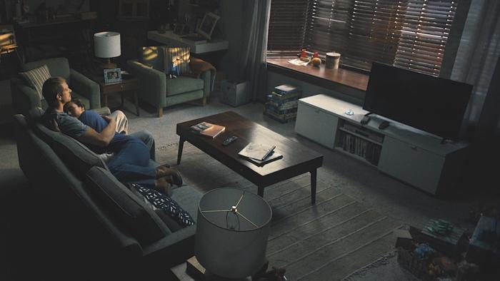 Silent Night Movie: Seen from above and behind, Brian Godlock (Joel Kinnaman) and his wife, Saya (Catalina Sandino Moreno), hold each other on the couch in a darkening living room