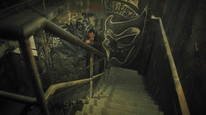 Silent Night Movie: Seen from above as he climbs a graffiti-covered staircase, Brian Godlock (Joel Kinnaman) keeps his gun raised, on guard and ready for anything
