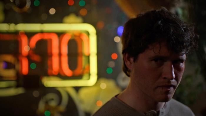 Silent Night, Deadly Night Movie: Billy Chapman, looking concerned, stands near a lit-up OPEN sign and Christmas lights