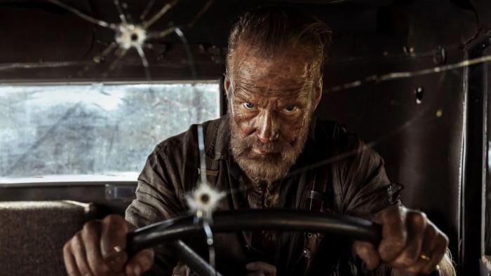 Sisu: Road to Revenge Movie: Seen through a bullet-hole-riddled windshield, Aatami Korpi (Jorma Tommila) drives furiously