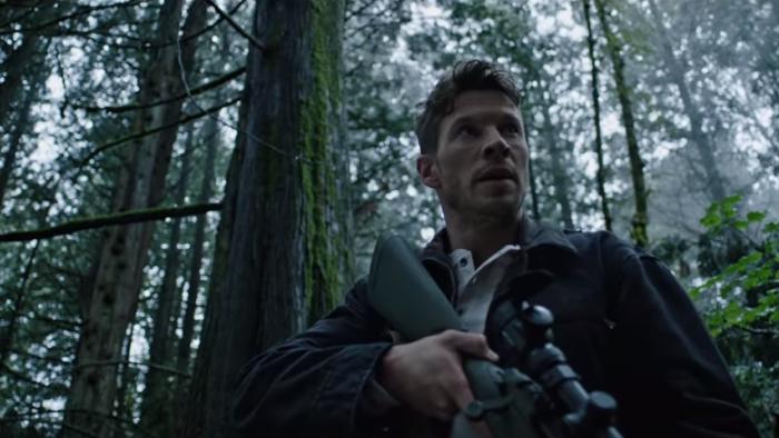 Sniper: Assassin's End: Chad Michael Collins stands in forest surrounded by trees holding rifle.