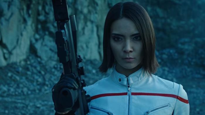 Sniper: Assassin's End: Sayaka Akimoto stands in white leather jacket holding large rifle