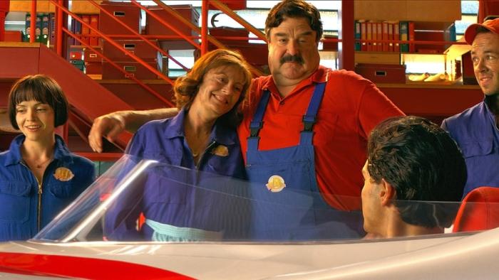 Speed Racer movie: Trixie, Speed's parents, and Sparky in mechanic outfits look at Speed, who's seated in a car