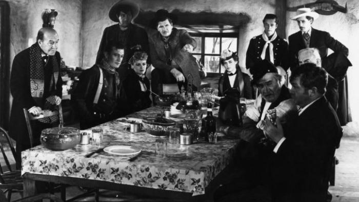Stagecoach movie: A group of adults gather around a dining table