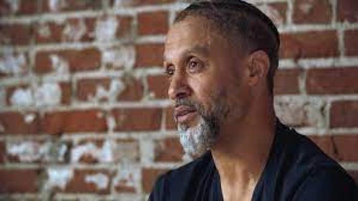 Stand: Against backdrop of brick wall, Black man center right looks left