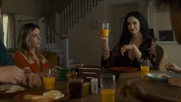 Stone Cold Fox movie: Krysten Ritter holds up an orange juice glass at a dining table, as if toasting Kiernan Shipka and others off screen