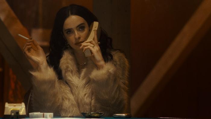 Stone Cold Fox movie: Krysten Ritter sits in a fur coat with a cigarette in her right hand and a phone up to her left ear