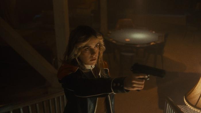 Stone Cold Fox movie: Kiernan Shipka holds a gun with two hands, pointing it at someone off screen