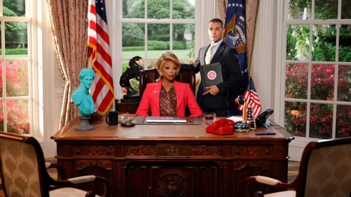 Stop! That! Train! movie: RuPaul, playing the president, sits at a desk in a facsimile of the Oval Office
