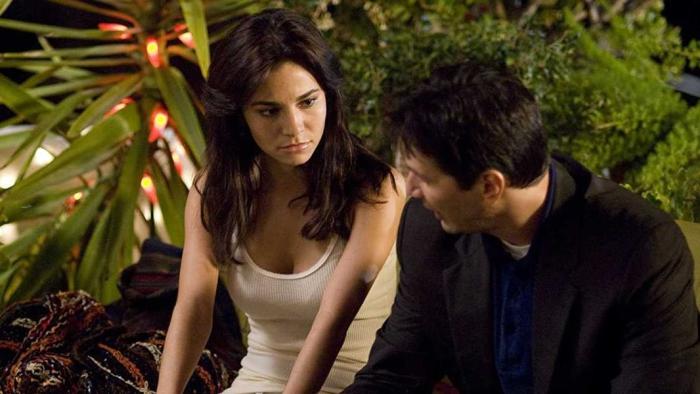 Martha Higareda and Chris Evans sit together next to some leafy plants. 