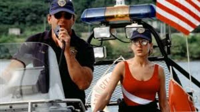 Striking Distance: Police officers on a boat, one uses a radio, with an American flag in the background.