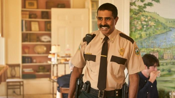 Super Troopers 3 Movie: Trooper in uniform stands in a room with a bookshelf and mural