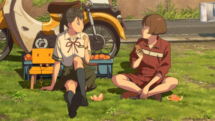 Suzume movie: Suzume sits with a friend in the grass, behind them is a yellow moped, two bins of oranges, and a chair.