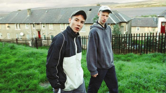 Sweet Sixteen: Two young White male teens in casual wear try to look cool and threatening as they walk through a housing estate