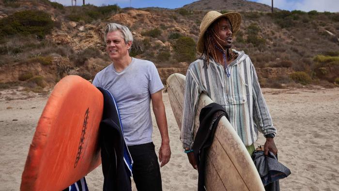 Sweet Dreams: Johnny Knoxville and Gate hold surfboards on a beach