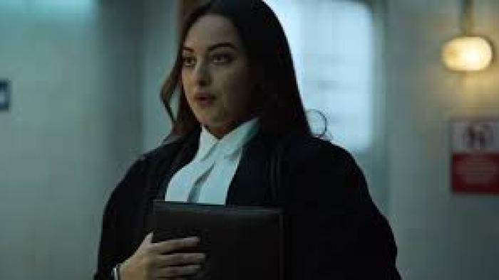 System movie: Indian woman in formal legal attire holding a folder, walking in a dimly lit hallway.