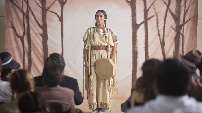 Te Ata Movie: Te Ata dressed in traditional Chickasaw clothing as she stands on stage