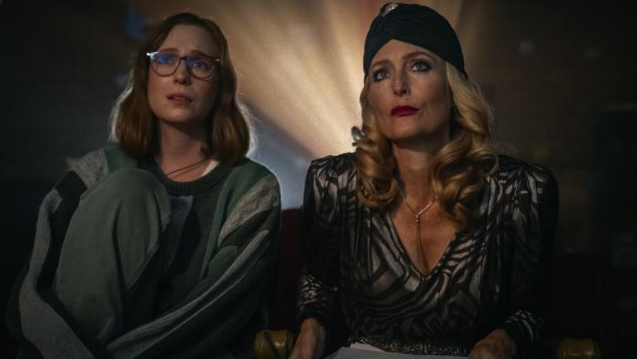 Teenage Sex and Death at Camp Miasma movie: Kris (Hannah Einbinder) and Billy Presley (Gillian Anderson) watch a movie, the projector behind them