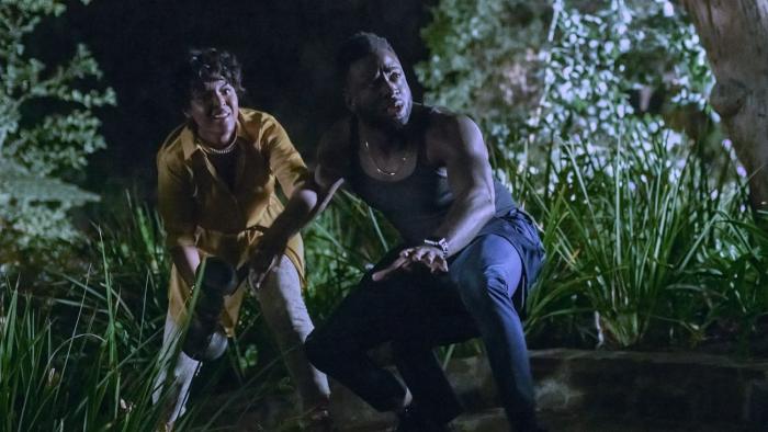 The Blackening Movie: Antoinette Robertson and Sinqua Walls crouch outside as they try to escape the killer