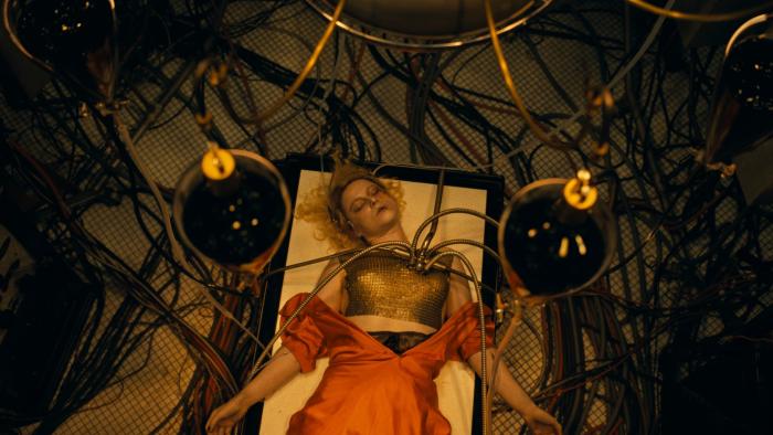 The Bride! Movie: Jessie Buckley lies unconscious on an operating table in an orange dress, with gold electrodes sitting on her heart