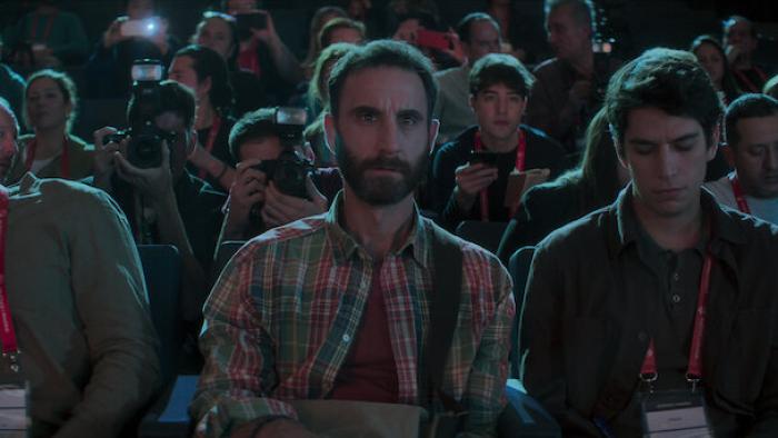 The Champion movie: Spanish bearded man in plaid shirt sits with other reporters and photographers at a press event