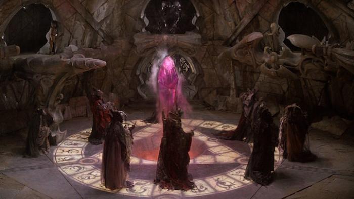 The Dark Crystal Movie: A group of hooded occultists stand around a large, glowing pink crystal inside a dark cave