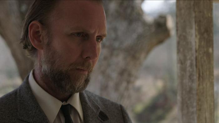 The Devil to Pay movie: a bearded white man in suit on left talks to someone off camera