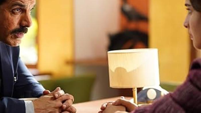 The Diplomat: Two people sitting across from each other at a table with a lamp between them