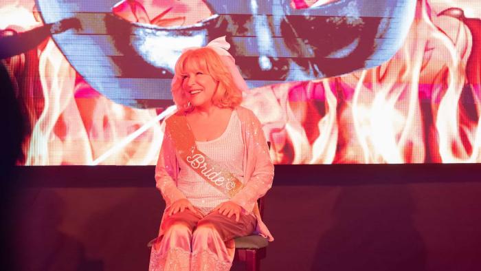 The Fabulous Four Movie: Bette Midler smiles while sitting on a stage wearing a sash that says "Bride"