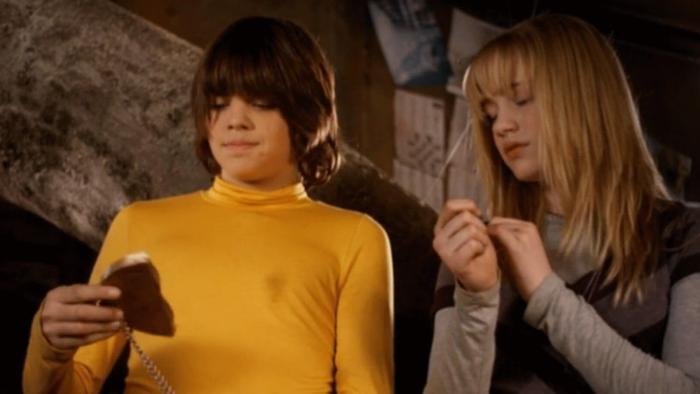 The Gold Retrievers movie: A boy in yellow mockneck and girl look down at a broken gold coin on a chain