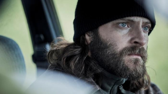 The Hanging Sun: Hitman John stares intensely out of a car window while wearing a beanie hat
