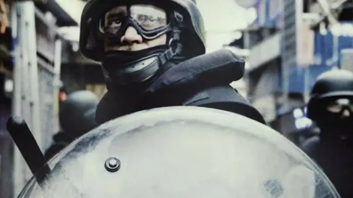 The Kitchen: A close-up of a policeman in riot gear, complete with shield and truncheon.