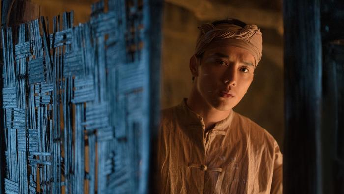 The Last Wife movie: Vietnamese man in tan shirt and headband stands in doorway on right