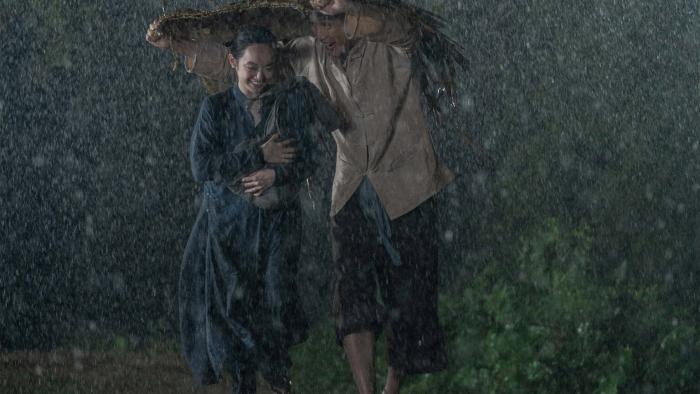 The Last Wife movie: Vietnamese man and woman center run in the rain under a straw mat