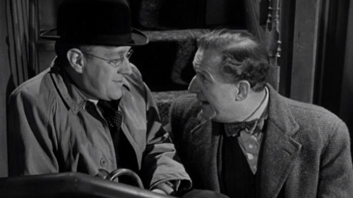 The Lavender Hill Mob: Two White men sit on stairs together wearing coats, hat, and one carries an umbrella