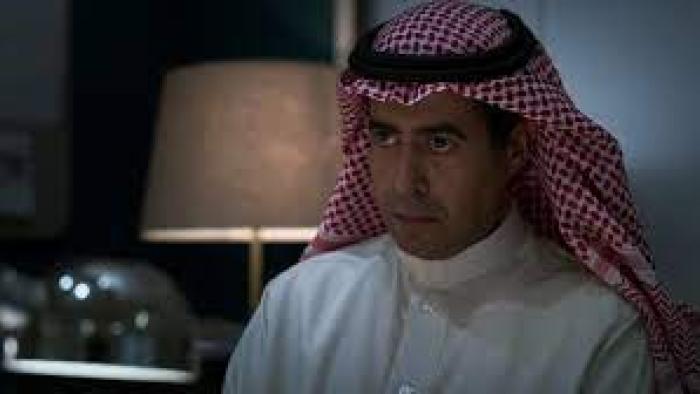 The Matchmaker: Saudi man in white shirt and red and white kaffiyeh sits at desk with lamp in background