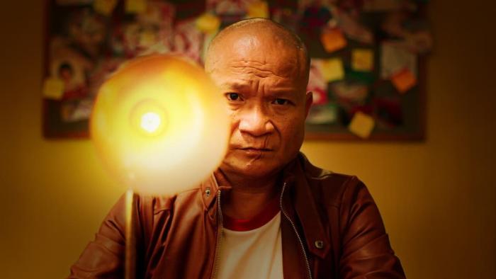 The Murderer movie: Thai man in red jacket center with lamp left faces camera