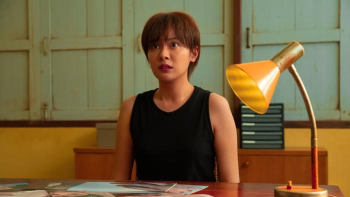 The Murderer movie: Thai woman in black tank top center sits at desk with lamp on right