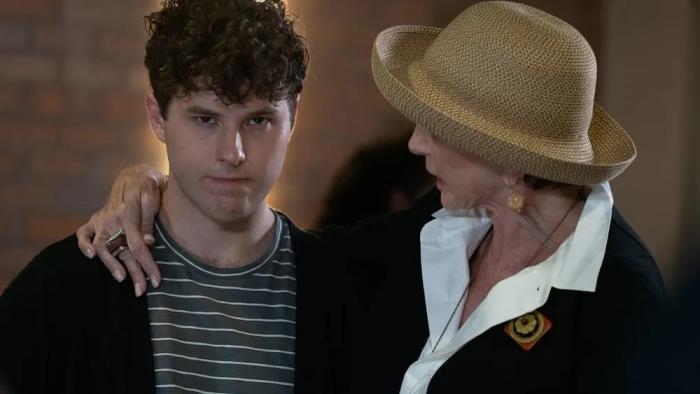 The Nana Project: A woman in a straw hat talks to an angry-looking young man with curly brown hair