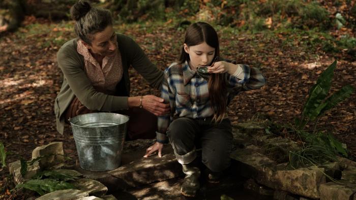 The Quiet Girl: A young girl and a middle-aged woman crouch beside a well