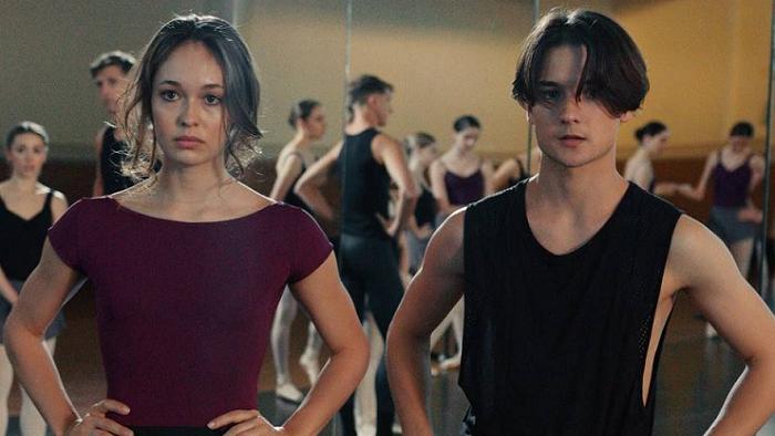 A young couple in a dance studio stand with arms akimbo and look frustrated and tired