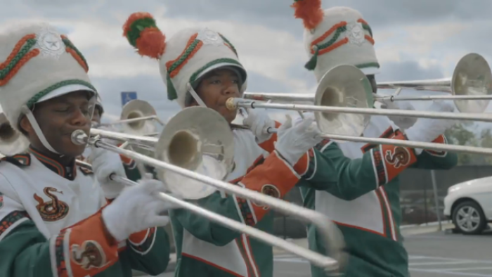 Still from The Return: Three African American Florida A&M University  marching band trombone players, wearing the school's green, orange, and off-white uniforms and headwear