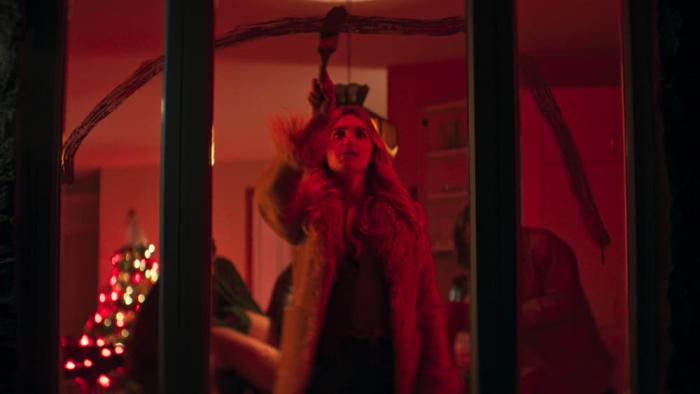 The Sacrifice Game movie: In red light filter, a white woman from the inside paints a red streak on a house window