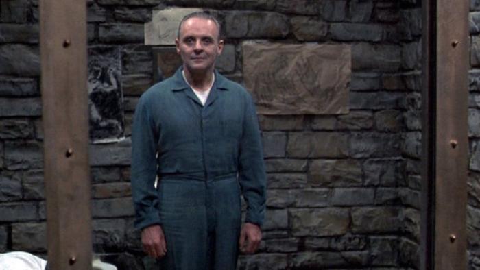 The Silence of the Lambs movie: Hannibal Lecter wears a blue jumpsuit and stands inside a brick cell