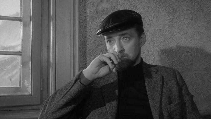 The Spy Who Came in from the Cold: A White man in a cap sits by a window while holding pen to his lips